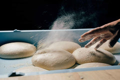 Pizza dough balls in proofing tray being dusted with flour