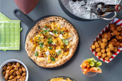 A pizza topped with fritos on a tabletop surrounded by snacks