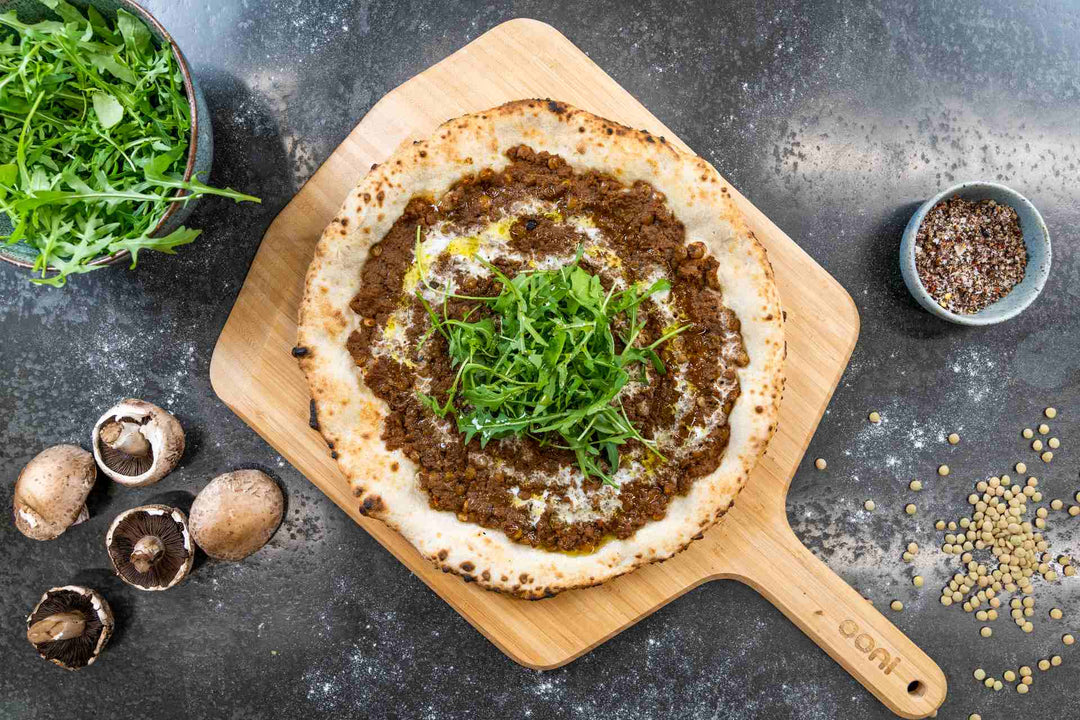 A pizza with mushroom ragu mince and rocket on top on a wooden pizza peel