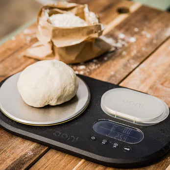 Ball of pizza dough on a set of scales, being used to measure pizza dough hydration.