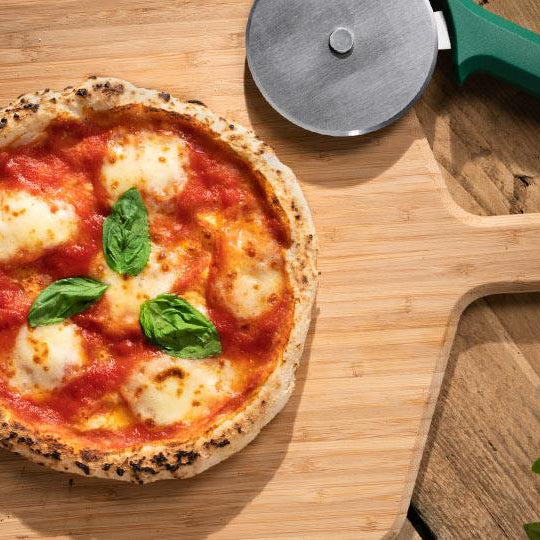 A pizza covered in cheese, tomato and basil on a wooden pizza peel baked using a Gluten-Free Pizza Dough recipe