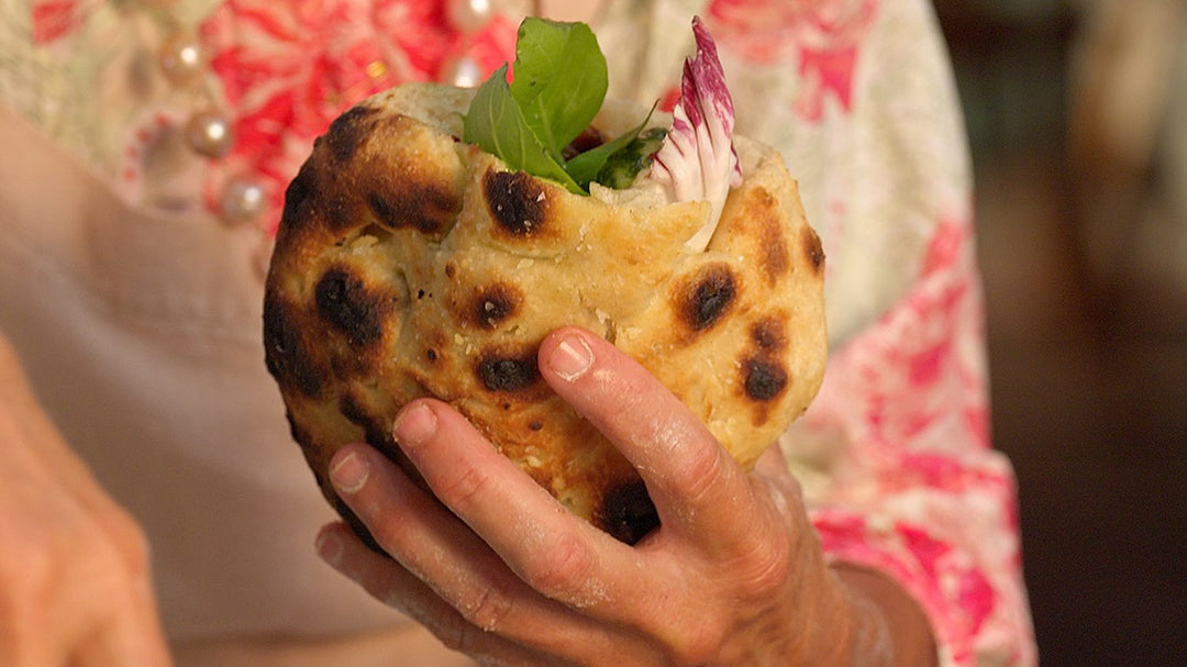 Hand holding a cooked pizzette stuffed with baby peppers, mozzarella, radicchio and basil.