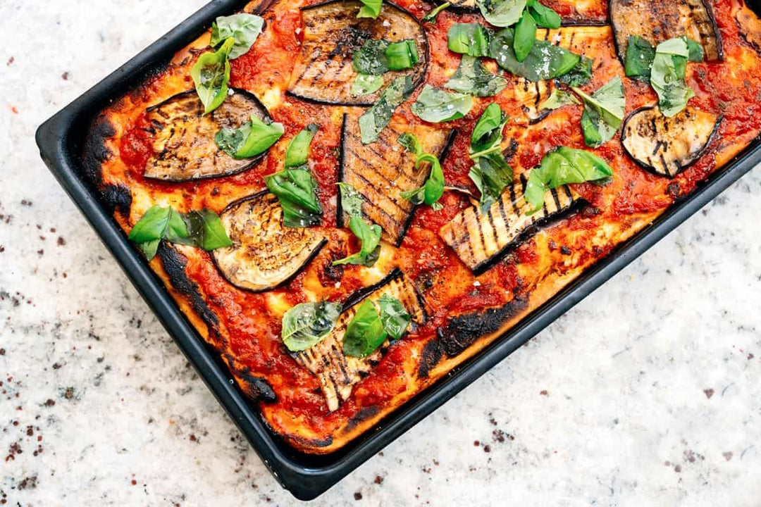 Pizza topped with tomato, aubergine and fresh basil in a metal sheet pan. Baked using a Sicilian pizza recipe.