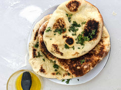 Sourdough naan breads stacked on a white plate topped with butter and coriander. Baked using a sourdough naan bread recipe.