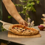 pizza being placed on bamboo pizza peel and serving board with wide turning peel 