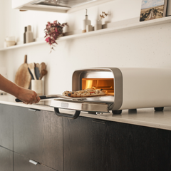 pizza being retrieved from ooni volt 2 electric pizza oven in polar white